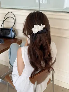 Vue détaillée d'une pince à cheveux fleurie en mousseline blanche et nœud satin noir