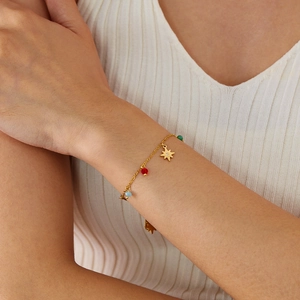 Detail of a gold chain bracelet with star pendant and colorful beads on a model's wrist