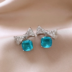 Macro view of crystal bow earrings featuring a large square blue drop stone on silk
