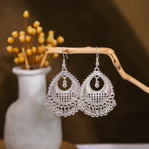 Detailed shot of ethnic silver earrings with hollow patterns and ball tassels on wood