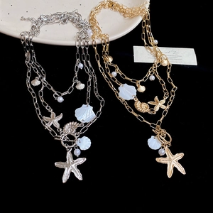 Close-up of bohemian layered necklace with starfish shell and pearl pendants on plate