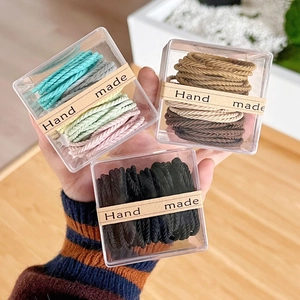 Detail of multi-colored braided elastic hair ties in a transparent gift box with handmade label