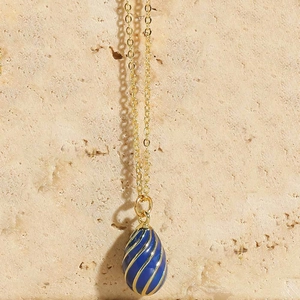 Close-up of blue enamel egg pendant with gold spiral lines on a gold chain necklace