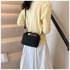 Model wearing a black crossbody bag with geometric texture and gold hardware on stairs