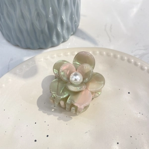 Floral acetate hair claw with pink gradient petals and a white pearl center on a ceramic plate