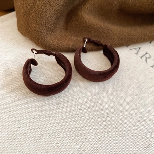 Gros plan de boucles d'oreilles créoles floquées marron foncé sur fond textile automnal