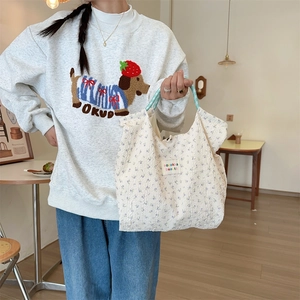 Floral canvas tote bag held by a model in a cafe setting, showing casual Korean style