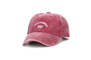 Dettaglio del ricamo bianco California 1987 su cappellino in cotone rosso lavato