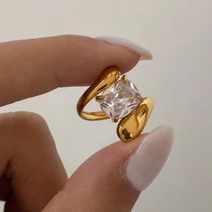 Detail of bypass gold plated ring featuring a large cushion cut clear gemstone setting