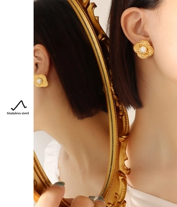Close-up of golden floral pearl earrings in stainless steel with a mirrored reflection