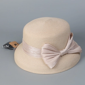 Dettaglio cappello di paglia beige con grande fiocco e ciondolo con lettera M