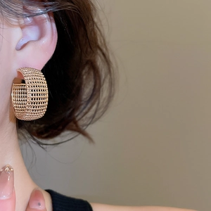 Macro shot of gold wide C-shaped hoop earrings with intricate mesh hollow-out design