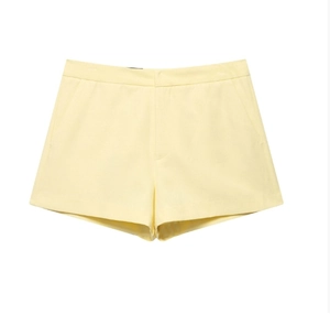 Detail of high-waisted pale yellow casual shorts with side pockets and smooth fabric
