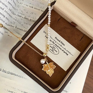 Detailed macro view of 18K gold maple leaf pendant with rhinestones and pearl accents