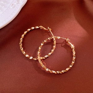 Detail of gold hoop earrings with textured diamond facets on red silk background