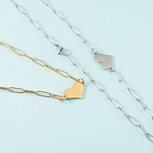 Golden and silver heart pendant necklaces with paperclip chains on blue background