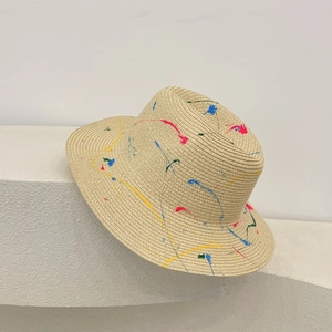 Detailed view of hand-painted colorful splatters on a beige woven straw Panama sun hat
