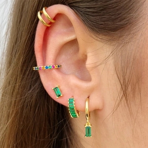 Close-up of bohemian gold layered earrings featuring emerald green crystals on a model