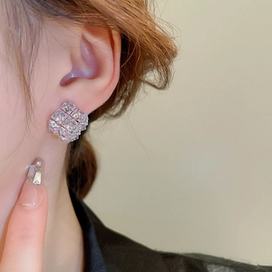 Close-up of geometric square zirconia stud earrings worn by a model in warm lighting