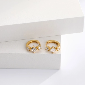 Detail of gold hoop earrings with square zircon stone and claw setting on white block