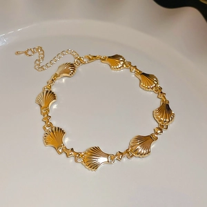 Top view of gold shell-shaped link bracelet with adjustable chain on a white ceramic plate