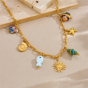 Golden ocean theme charm necklace with ceramic fish and shell pendants on stone