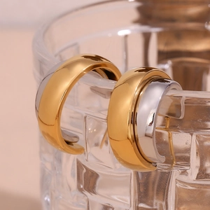 Detail of C-shaped mixed gold and silver earrings on a glass rim with a mirror finish