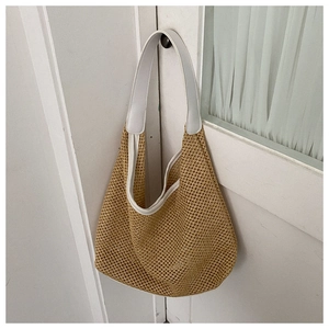 Detail of khaki woven straw tote bag with white PU leather strap hanging on a white door