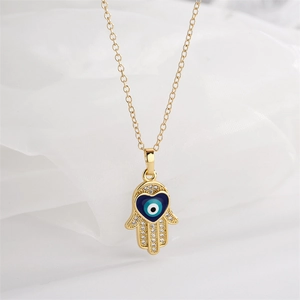 Close-up of golden Hamsa hand pendant with blue heart evil eye on white fabric