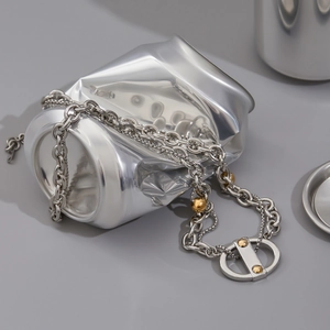 Gros plan d'un collier bicolore argent et or exposé sur une canette de soda écrasée