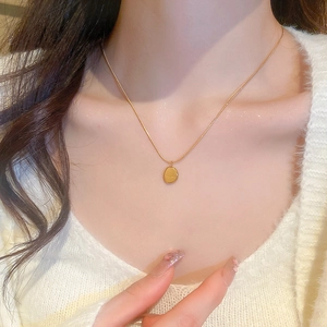 Gros plan d'un collier doré avec pendentif ovale porté par un mannequin
