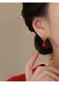 Detail of elegant hollow flower earrings with red bead pendant worn by a model