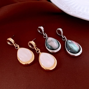 Detail view of water drop shell earrings in gold and silver finishes on red fabric