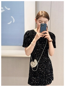 Detailed close-up of a silver shell-shaped metallic clutch bag with sequined dress texture