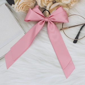 Detail of pink satin ribbon bow hair clip with elastic band on a soft plush background