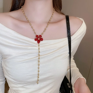 Detail of a vintage-style Y-shaped long necklace with a red flower pendant and gold beads