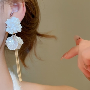 Macro shot of elegant white petal flower tassel earrings worn by a model in warm light