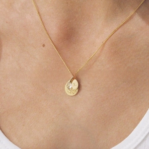 Detail of a gold-tone necklace with a letter L charm and subtle rhinestone pendant
