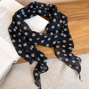 Detailed macro shot of a black polka dot silk scarf necklace draped over an art book