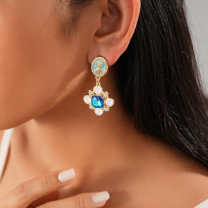 Close-up of bohemian gold drop earrings with blue enamel and crystal gems on model