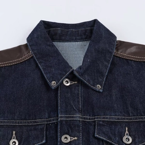 Vue détaillée de la veste en jean bleu foncé avec patchwork en cuir brun et boutons en métal
