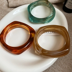 Close-up of multicolored chunky acrylic resin bangles in amber and teal in a ceramic dish