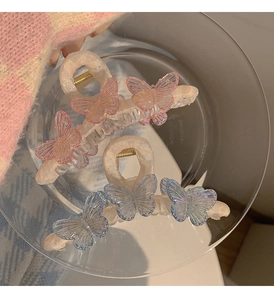 Detail view of large butterfly hair clips with pink and blue jelly gradients in a glass dish