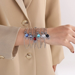 Dettaglio di bracciali Hamsa argentati con pietre colorate indossati su un blazer beige