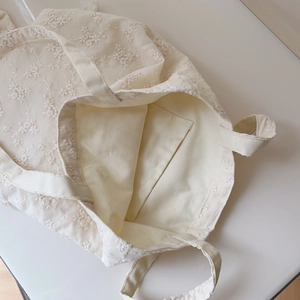 Close-up of floral embroidery on cream cotton tote bag showing the interior pocket