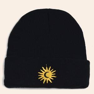 Detail shot of black knitted beanie featuring yellow sun and moon embroidery texture