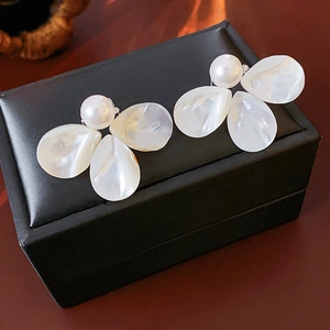 Detail of pearl flower earrings on a black leather jewelry box with shell texture