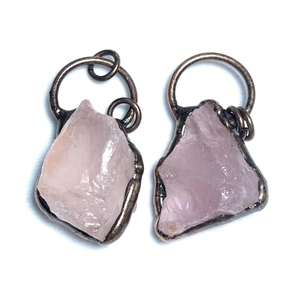 Dettaglio di ciondoli in quarzo rosa grezzo con bordi in bronzo vintage su sfondo bianco