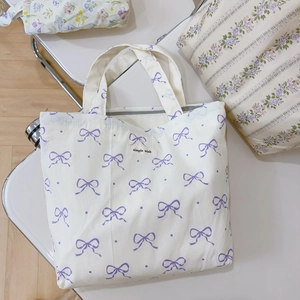 Close-up of a white canvas tote bag featuring purple bow patterns and Simple Wish label