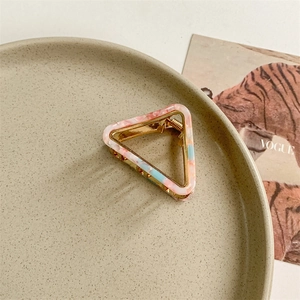 Macro detail of triangle acetate hair claw with pink marble texture and gold metal frame
